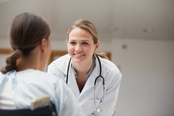 Smiling doctor looking at a patient on a wheelchair in hospital hallway-1